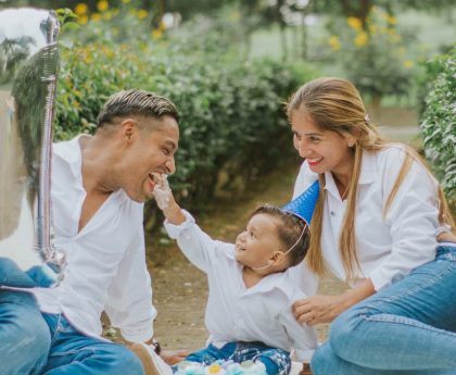 A joyful family celebrating their child's first birthday outdoors with cake and balloons.